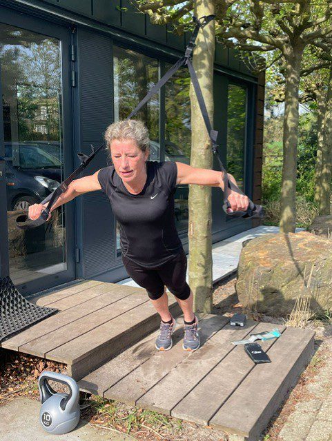 Oudere fitte dame in sportkleding traint met een TRX in haar tuin