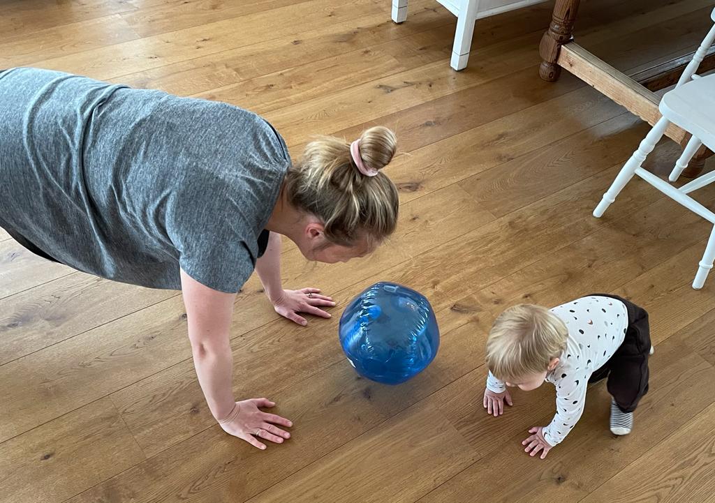 Moeder in sportshirt traint in huiskamer, in het bijzijn van haar jonge dochtertje