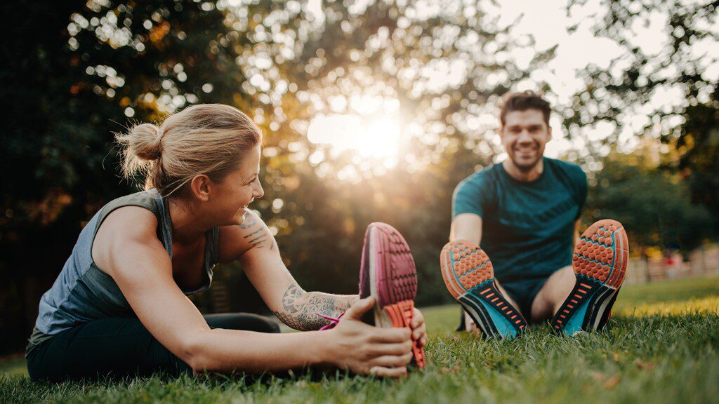 Vrolijke, lachende man en vrouw stretchen hun spieren voor of na een training.