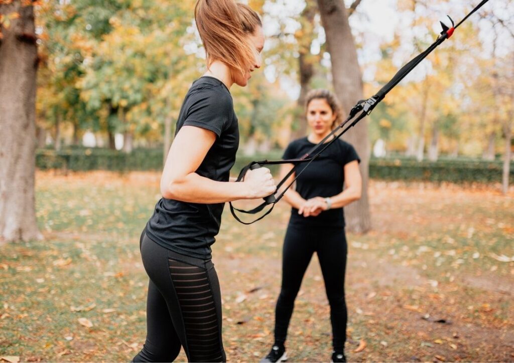 Vrouwelijke personal trainer traint vrouw in een bos. Dame traint met TRX