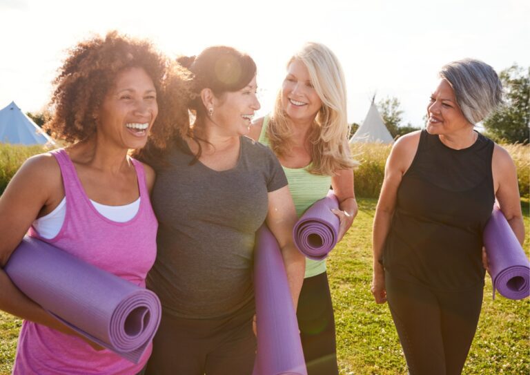 4 oudere dames in sporkleding, met een yoga matje onder arm, hebben lol met elkaar