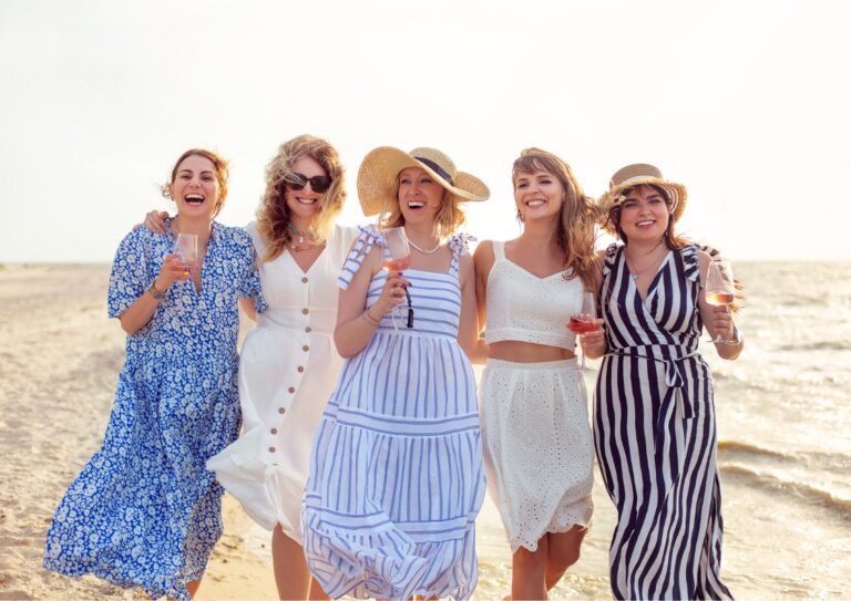 5 lachende dames op het strand met een glas wijn in de hand